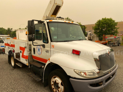 International 4300 bucket truck with a boom lift, white with orange stripe, showing side text and numbers on cab and body.