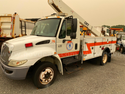 International 4300 bucket truck in-service showing side view with bucket lift and orange safety stripes.
