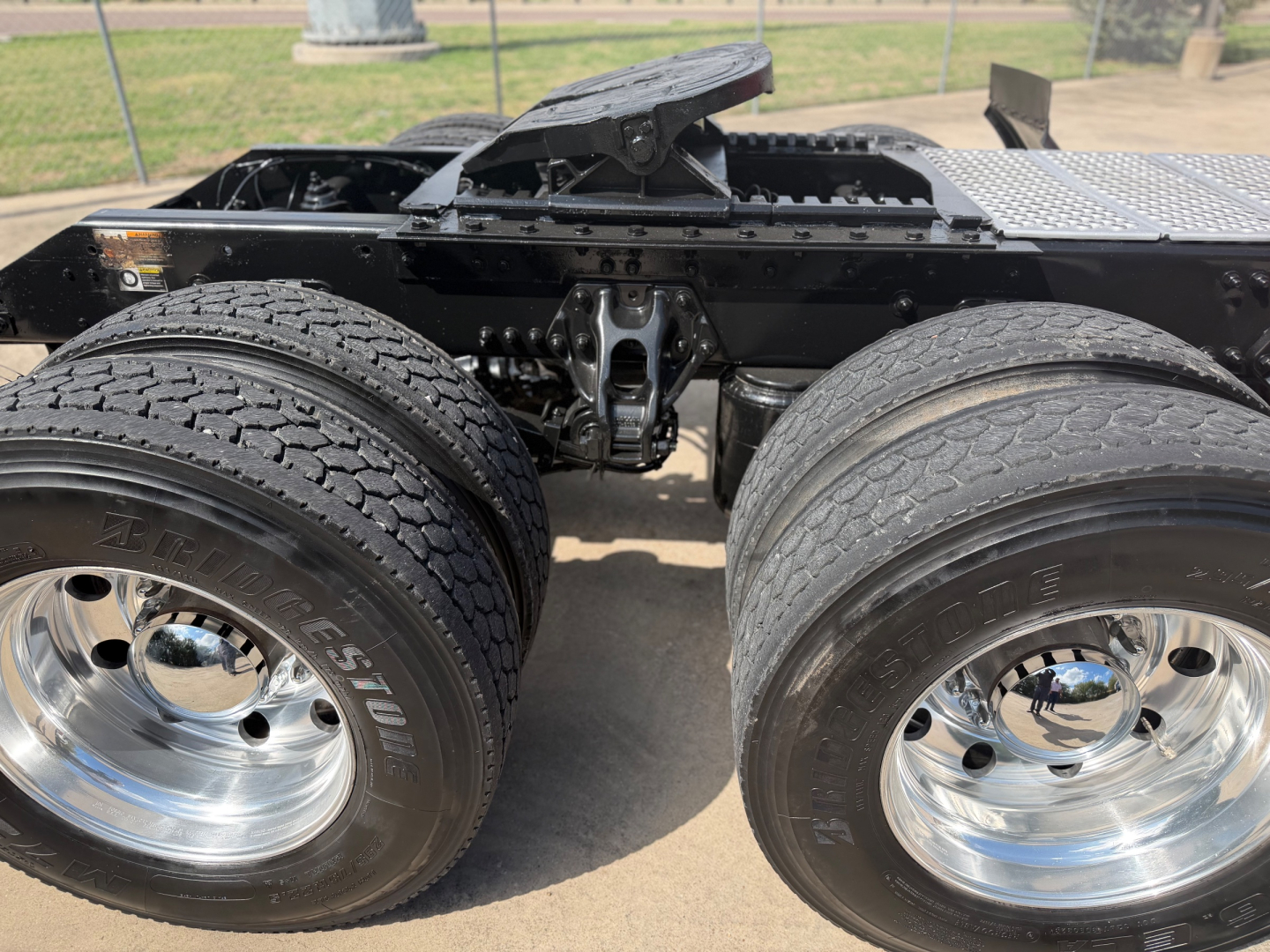 Kenworth T680 chassis showing dual rear axles with polished metal wheels and tires, frame rails, and mounting hardware.