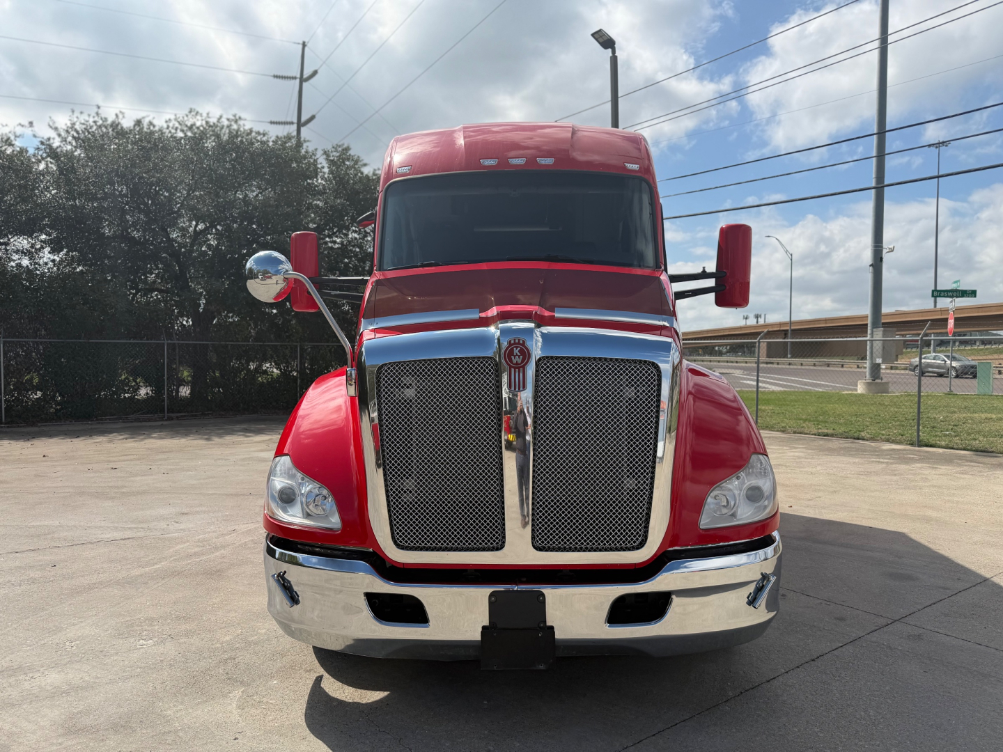 Kenworth T680 front view showing large chrome grille, red paint, dual hood mirrors, and bumper with license plate area.