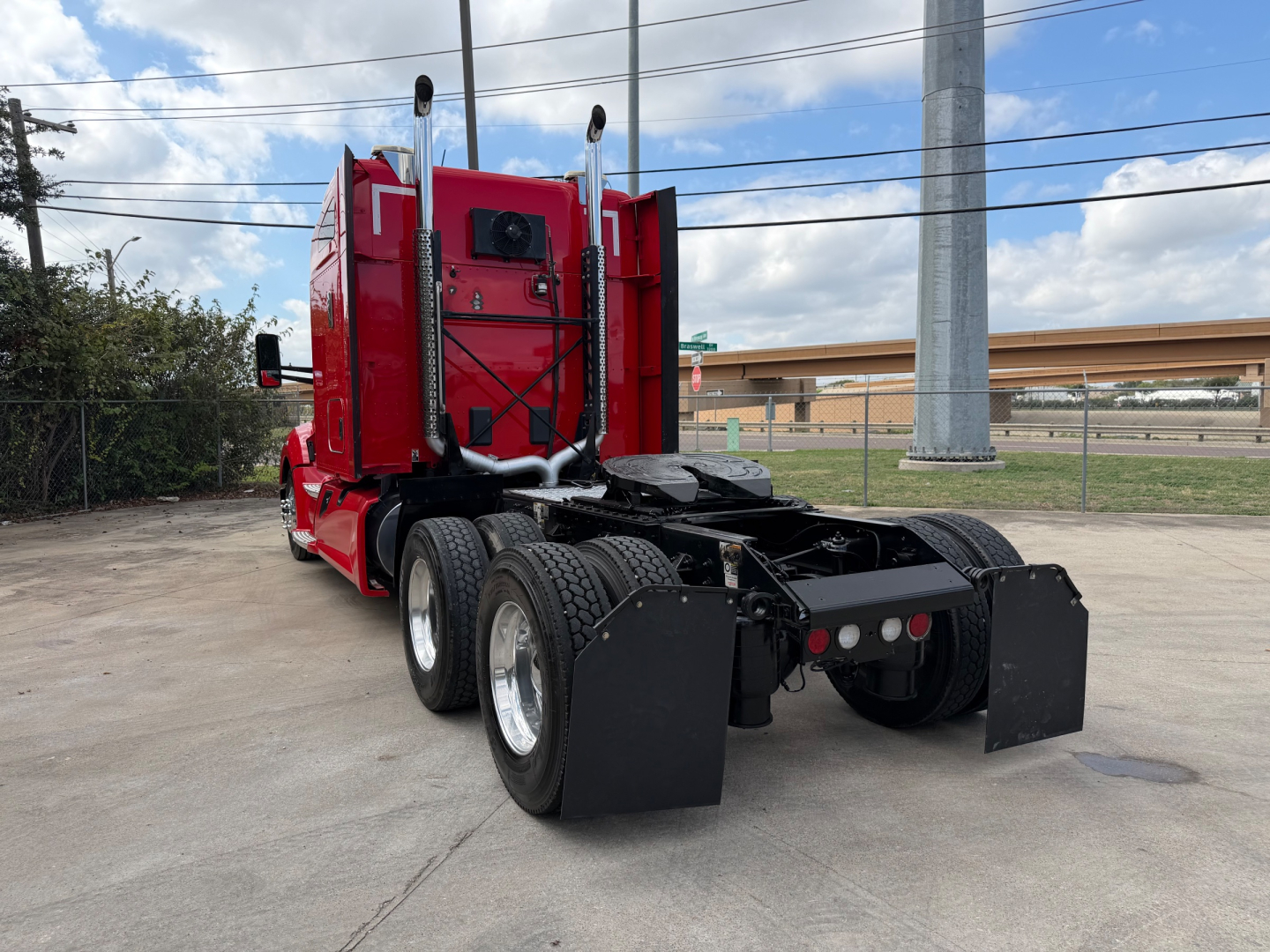 Kenworth T680 rear view showing dual rear axles and fifth-wheel coupling, red cab, black fenders, and mud flaps.