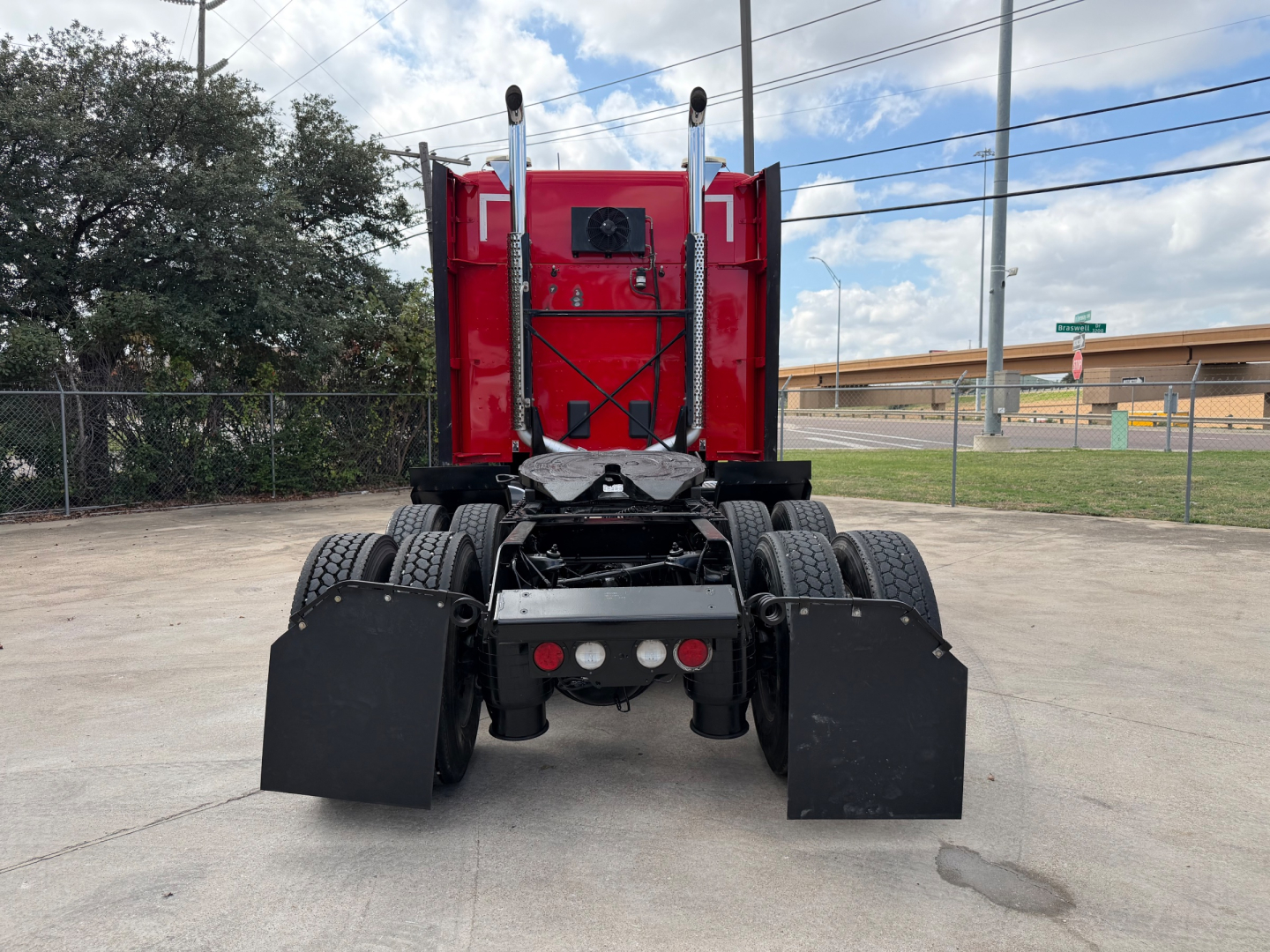 Kenworth T680 rear view showing fifth wheel and dual rear axles with mud flaps and red cab, no obvious text visible.