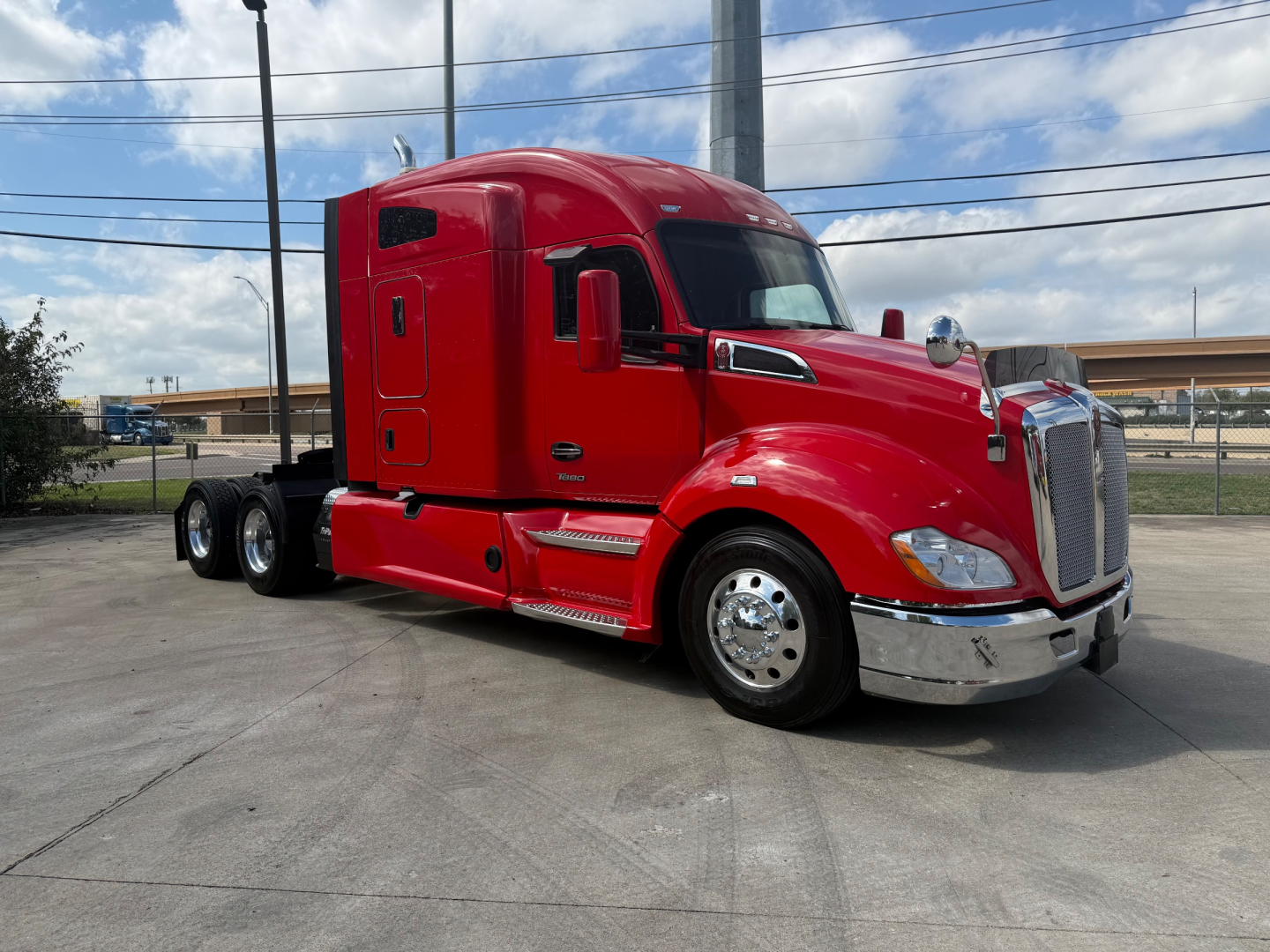 Kenworth T680 tractor in red, side view showing aerodynamic cab, chrome bumper, dual rear axles, and large fuel tanks.