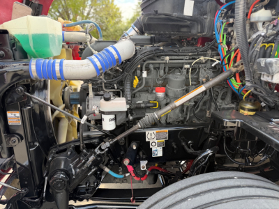 Kenworth T680 engine bay with numerous hoses, wiring, and components visible; coolant reservoir, air intake hoses, and various labels present.