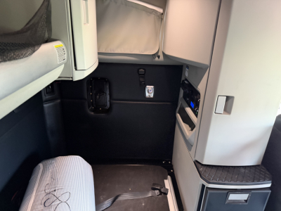 Cab interior of a Kenworth truck showing a small black panel and storage compartments with gray doors. Text visible includes a small label or badge near the doorway.