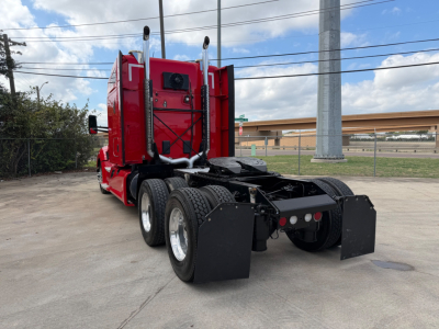Kenworth T680 rear view showing dual rear axles and fifth-wheel coupling, red cab, black fenders, and mud flaps.