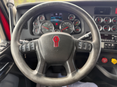 Kenworth truck steering wheel with Kenworth emblem and dashboard gauges visible in the cab interior.