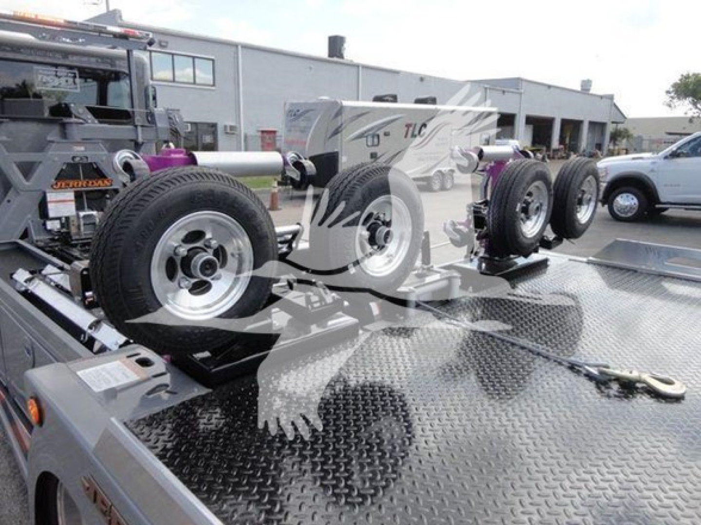 Truck bed with multiple spare wheels and a metal diamond plate surface, part of a rollback tow truck setup.