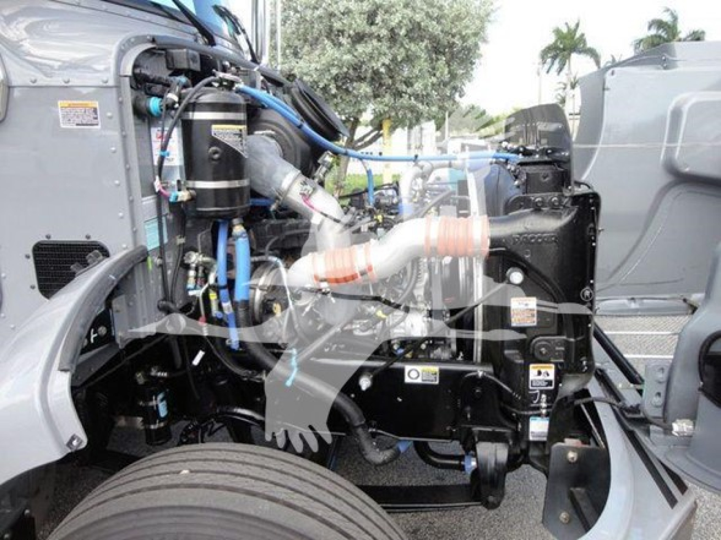 Peterbilt 337 engine bay with visible hoses, filters, and intake manifold in a rollback truck. Side of cab and front wheel visible.