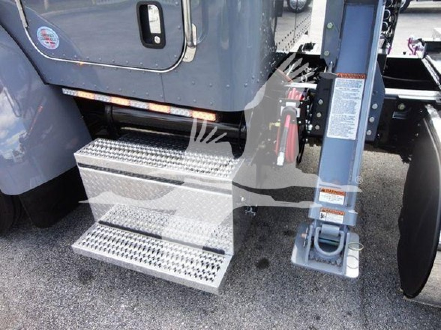 Peterbilt 337 rollback truck side step view showing aluminum diamond-plate steps and hydraulic system near cab access, with part of the wheel and blue chassis.
