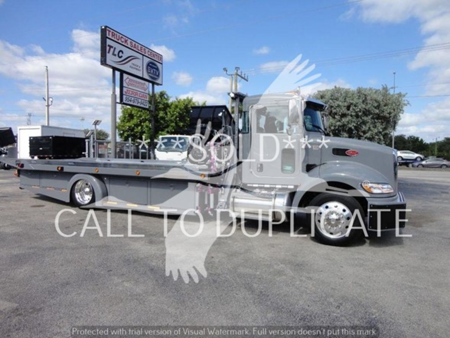 Peterbilt 337 rollback tow truck side view showing cab and long flatbed with TLC sign in background.