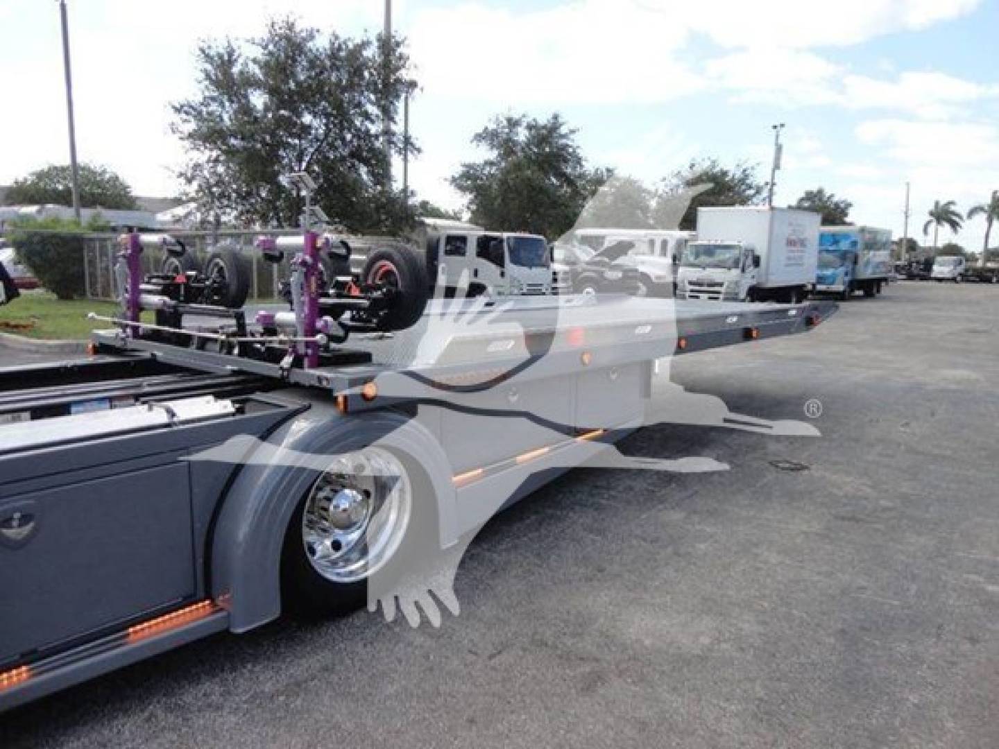 Peterbilt 337 rollback truck with trailers in background showing long flatbed and equipment carriers.