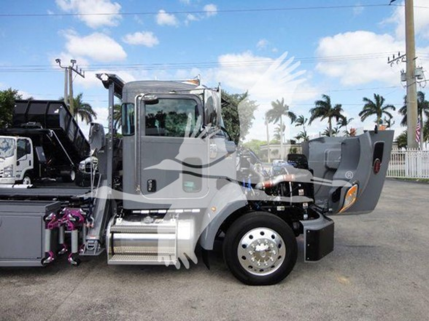 2022 Peterbilt 337 rollback truck side view showing cab doors open, chrome fuel tanks, steps, and rear dolly area.