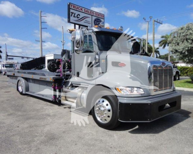2022 Peterbilt 337 rollback truck front-left view showing chrome grille, cab, and flatbed with equipment; TLC Truck Sales Center sign in background.