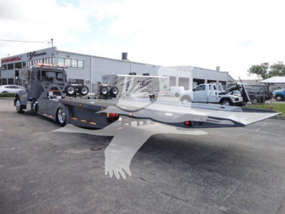 Peterbilt 337 rollback truck with a low-loader flatbed trailer in a dealership lot.
