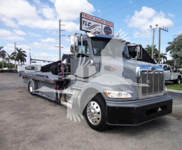 Peterbilt 337 rollback tow truck in a dealership lot, front-right view, metallic gray cab and flatbed with chrome bumper and dual rear axles.