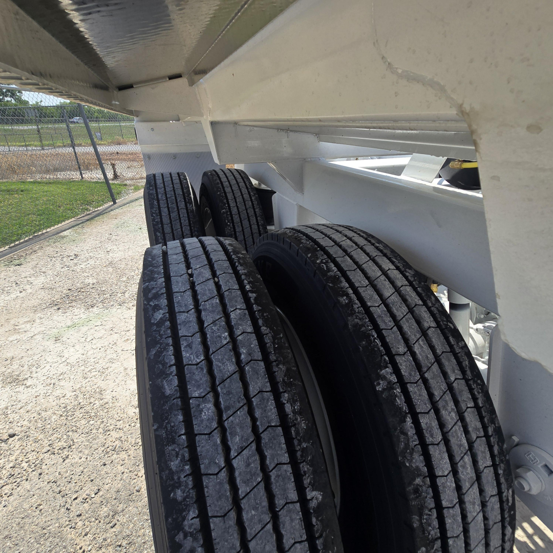 Trailer axle area showing dual rear tires and undercarriage of a dump trailer with white painted frame.
