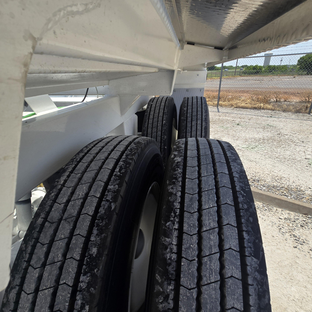 Dual rear axles of a trailer showing tires and undercarriage with metal beams.