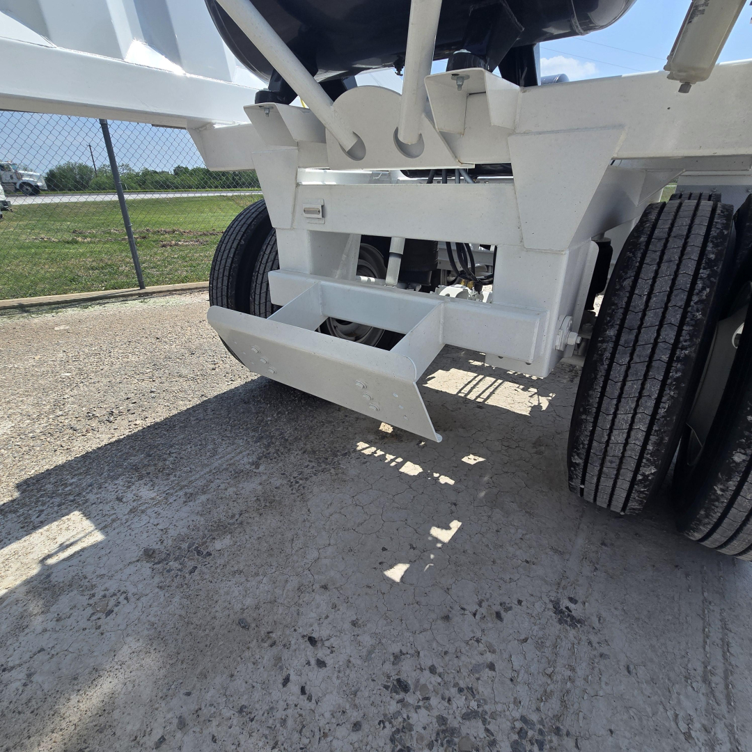 Dump trailer rear showing air ride suspension and bumper assembly undercarriage, white paint, dual rear wheels, concrete ground.