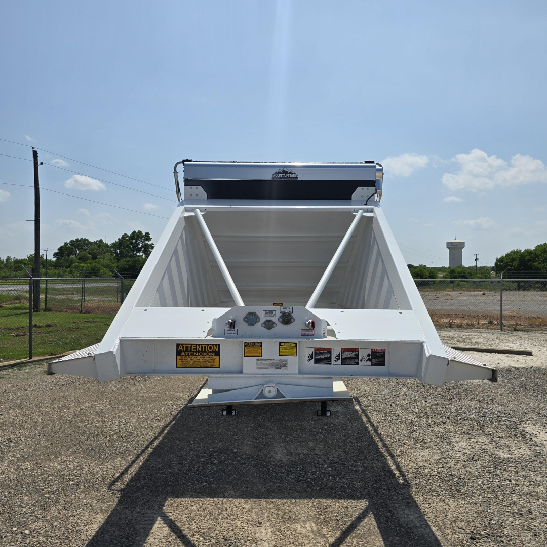 Dump trailer bed rear view showing white Steel structure and hydraulic air ride components with warning labels and hitch.