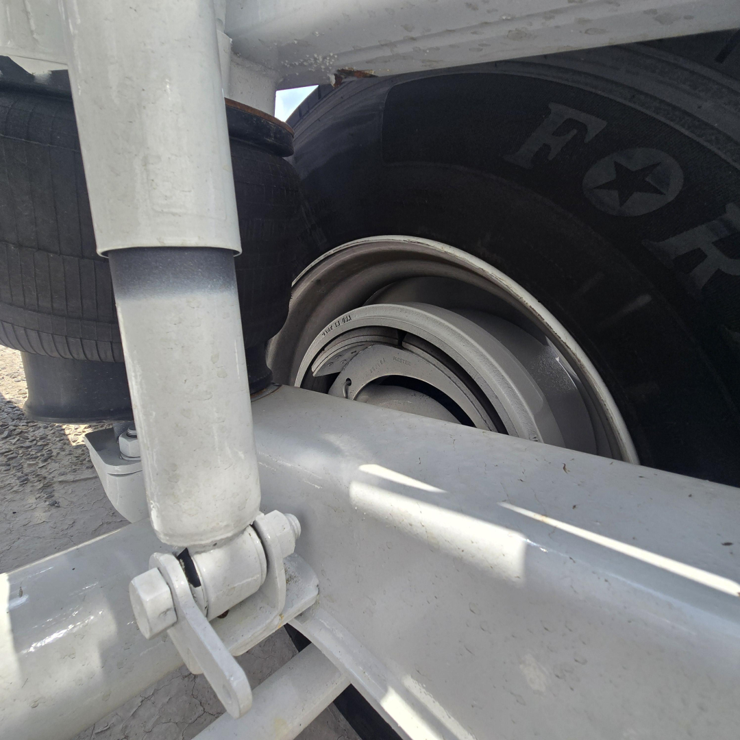 Trailer wheel hub and suspension components of a dump trailer showing a wheel with a visible rim and bolt assembly, leaf spring area, and part of the frame.