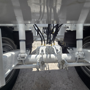 Trailer undercarriage showing air suspension lines and center axle with hoses and leaf springs. No visible text on components.