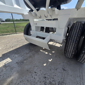 Dump trailer rear showing air ride suspension and bumper assembly undercarriage, white paint, dual rear wheels, concrete ground.