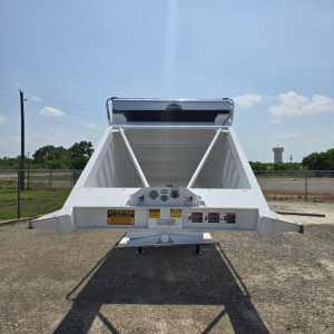 Dump trailer bed rear view showing white Steel structure and hydraulic air ride components with warning labels and hitch.