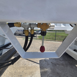 Inline valves and fittings on a trailer frame with hoses and a red-tipped control knob visible.
