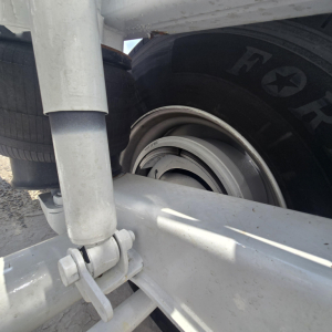 Trailer wheel hub and suspension components of a dump trailer showing a wheel with a visible rim and bolt assembly, leaf spring area, and part of the frame.