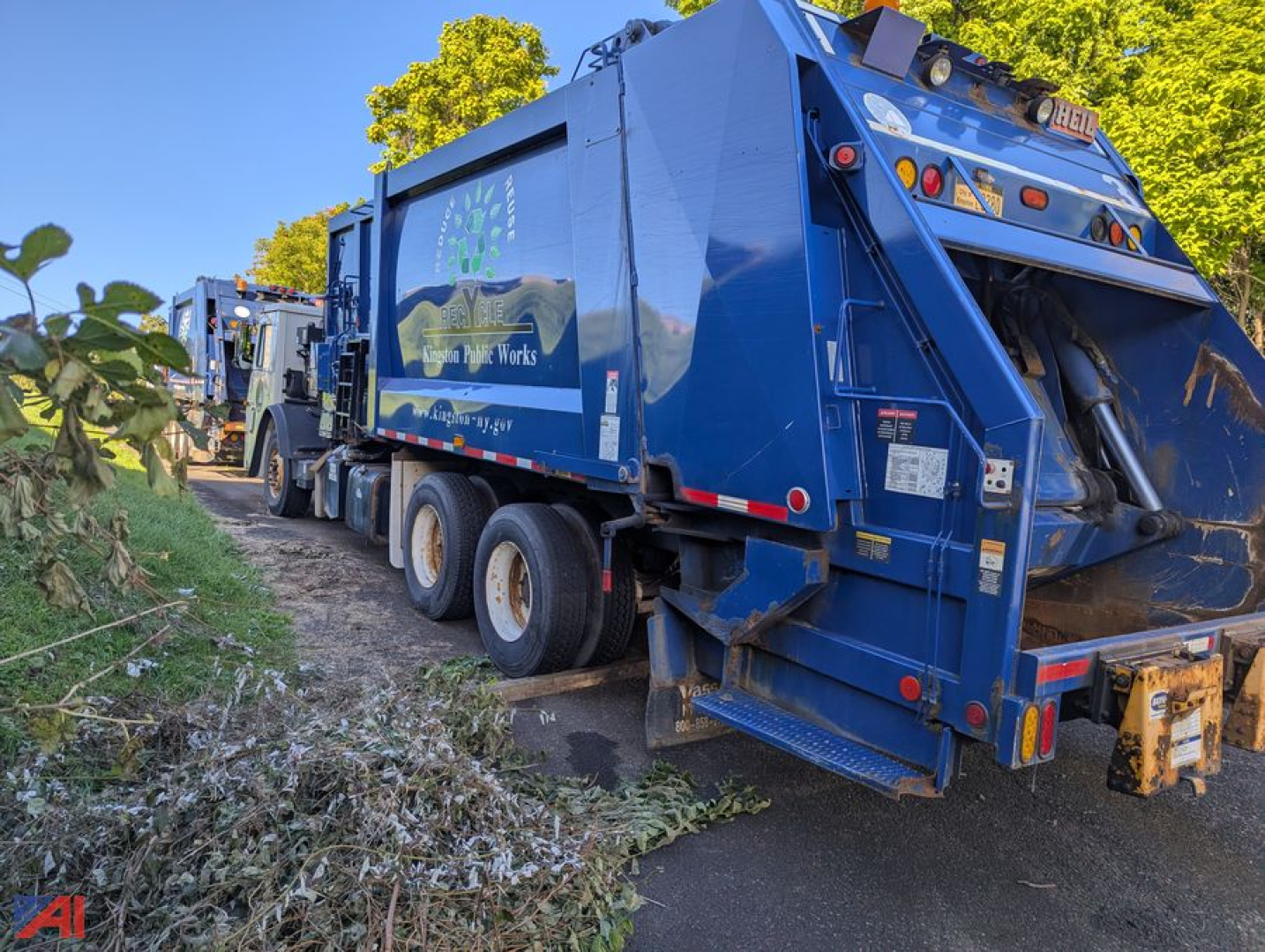 Rear and side view of a blue Mack TerraPro LEU613 refuse truck with compactor, three axles and graphic side panel.
