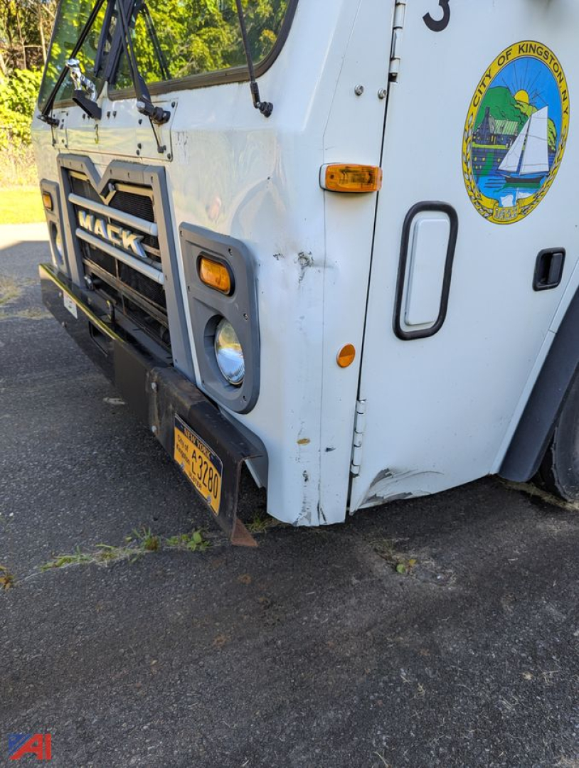 Front left corner of a white Mack TerraPro truck showing bumper, grille with MACK, round headlight, license plate, side marker, and City of Kingston seal on door.