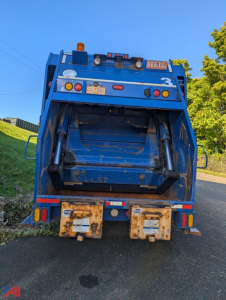 Back view of a blue 2011 Mack LEU TerraPro dump truck with rear ejector, visibility of hydraulic cylinders and tailgate hooks.