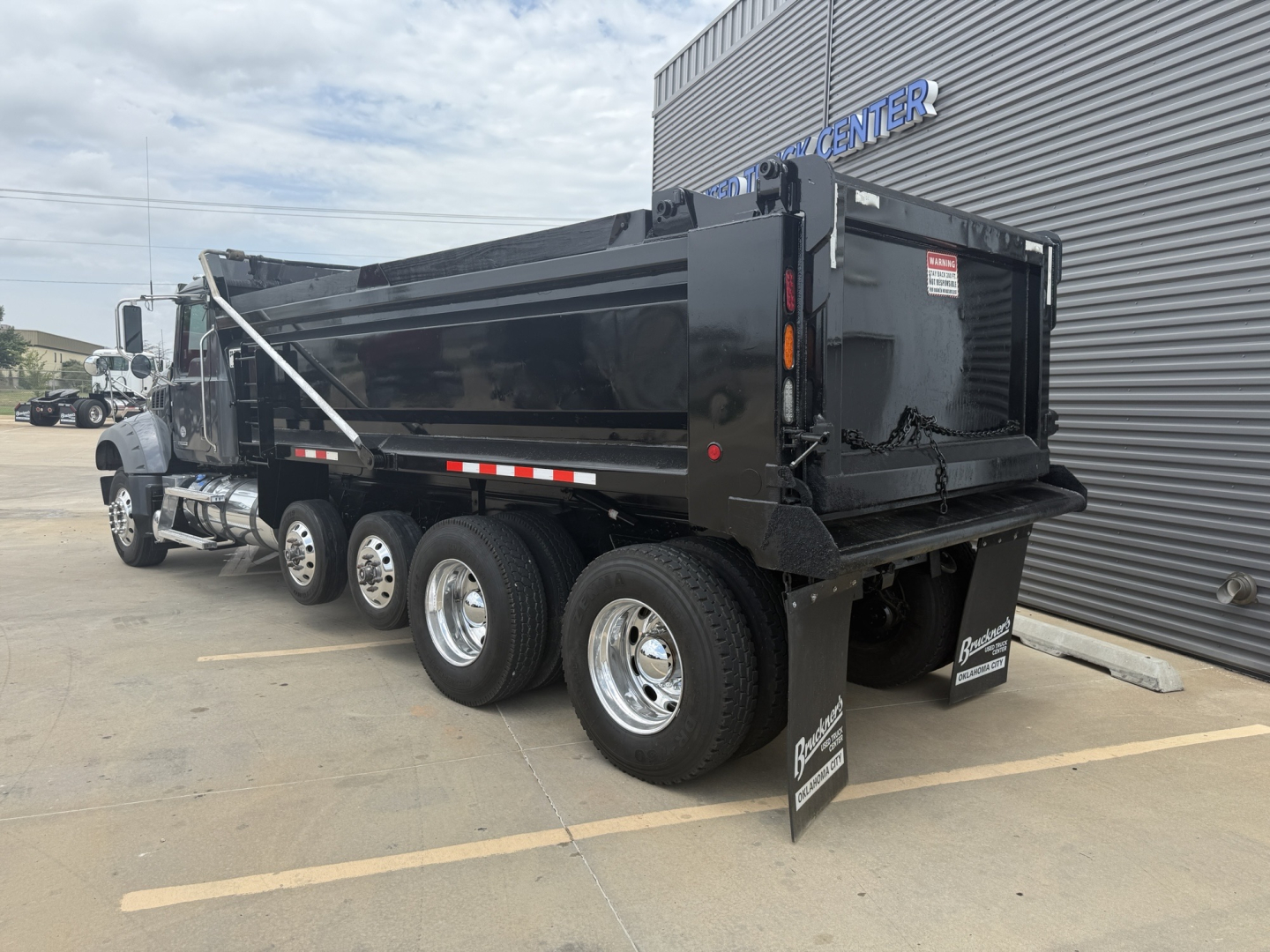 2023 Mack GR64F dump truck with rear dump body, side view showing dual rear axles, black paint, chrome wheels, and safety reflectors.