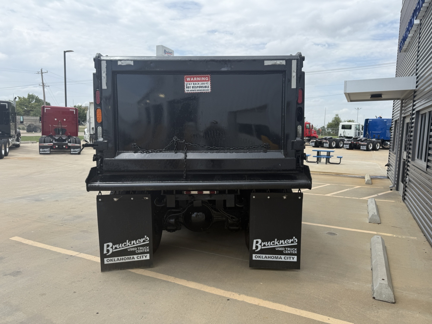 Dump truck bed of a 2023 Mack GR64F viewed from rear showing black dump body, tailgate, and two mud flaps with Buckner's Oklahoma City branding.