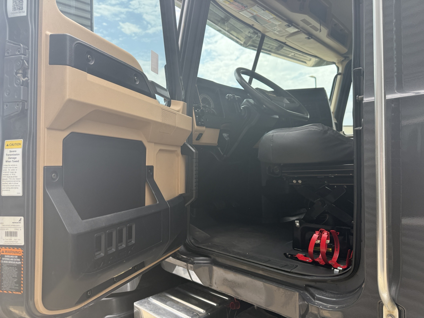 Cab interior of a 2023 Mack GR64F dump truck showing driver's seat, steering wheel, and entry area with safety strap visible.