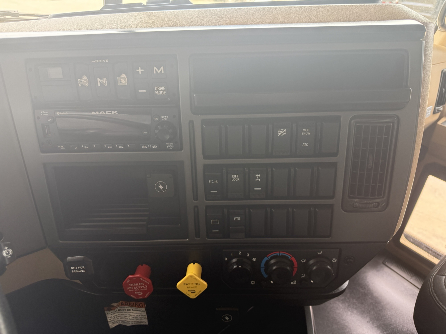 Dashboard of a 2023 Mack GR64F dump truck showing steering column area, HVAC controls, media unit, and ignition area with warning labels.