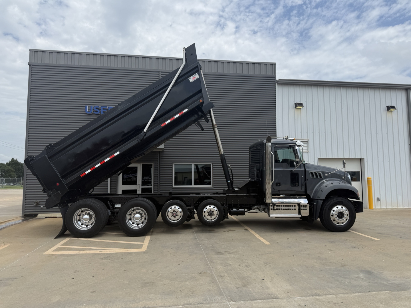 Dump truck with black cab and a raised dump bed showing side view of the Mack GR64F. Visible text on truck includes no obvious logos or stickers readable from distance.
