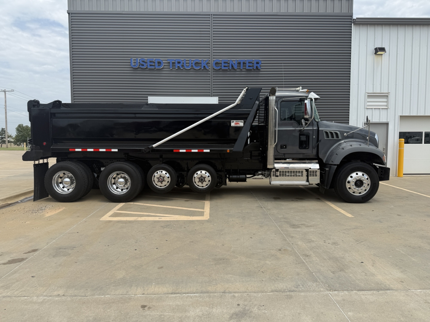 Mack GR64F dump truck side view showing dump bed and six wheels in front of a used truck center.