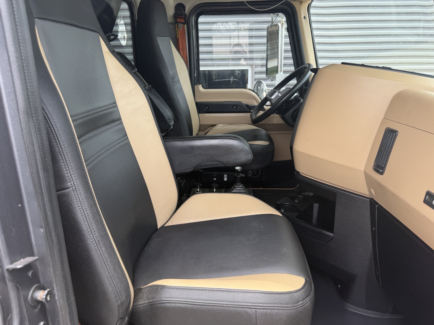 Interiors of a Mack GR64F dump truck cab showing front seats and dashboard. Beige and black seats with light tan dashboard panel; steering wheel and door panel visible.