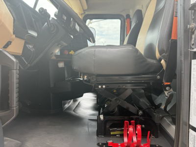 Cab interior of a 2023 Mack GR64F dump truck showing the driver seat, dash, and red suspension components under the seat area.