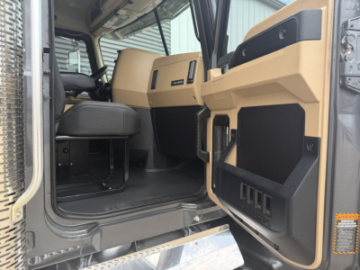 Cab interior of a 2023 Mack GR64F dump truck showing tan and black dashboard area and entry door with storage panels.