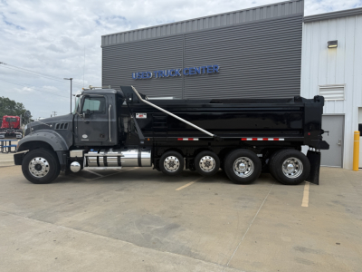 Dump truck showing a Mack GR64F dump truck with black body and multiple rear axles parked in front of a building labeled USED TRUCK CENTER.
