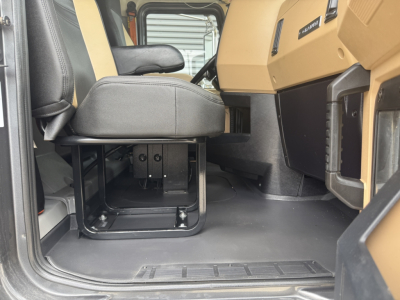 Cab interior of a Mack GR64F dump truck showing driver seat and floor area with metal pedestal and beige dashboard panel.