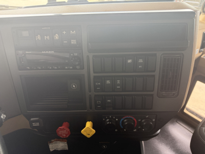 Dashboard of a 2023 Mack GR64F dump truck showing steering column area, HVAC controls, media unit, and ignition area with warning labels.