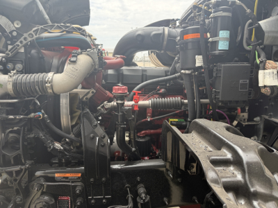 Engine bay of a 2023 Mack GR64F dump truck showing V-shaped exhaust, hoses, and various hydraulic lines