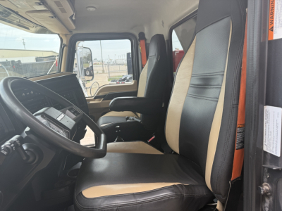 Cab interior of a 2023 Mack GR64F dump truck showing black and tan two-tone seats, steering wheel, and front controls.
