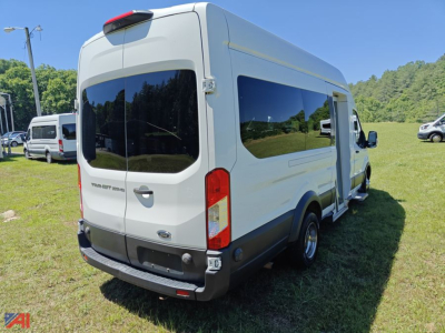 Ford Transit cargo van with wheelchair lift, rear and side views, white exterior, large windows, parked on grass.