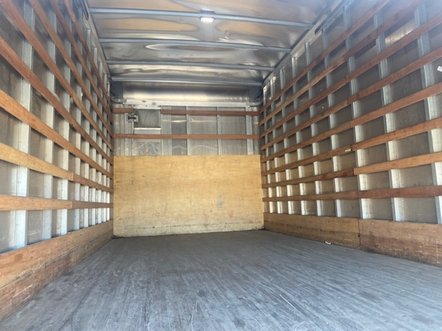 Truck box interior showing metal walls with wooden slats and a plywood bulkhead at the far end.