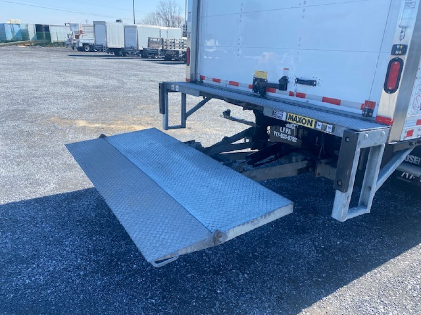 Rear of a Ford F-550 box truck with a lowered aluminum loading ramp extended from the back, showing the bumper and rear lights.